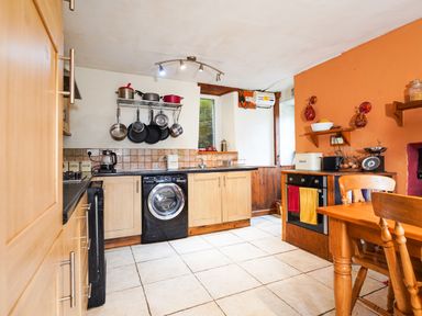 A kitchen with wooden cabinets hanging pots and pans a washing machine and a dining table at Delfryn Goginan in Goginan near Aberystwyth