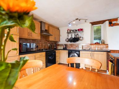 A kitchen with wooden cabinets black appliances hanging pots on a rack and a wooden dining table at Delfryn Goginan in Goginan near Aberystwyth