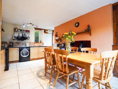 A kitchen with wooden cabinets a dining table with chairs and sunflowers on the table at Delfryn Goginan in Goginan near Aberystwyth