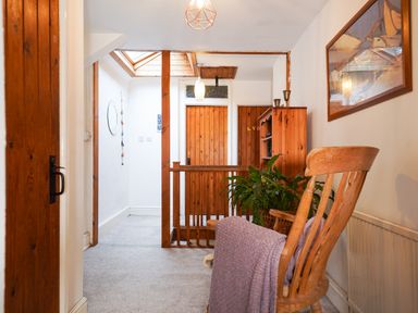 A hallway with wooden doors and beams a wooden rocking chair a plant and a bookshelf at Delfryn Goginan in Goginan near Aberystwyth