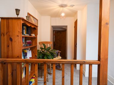 A hallway with wooden bookshelf and chair with a plant near wooden doors at Delfryn Goginan in Goginan near Aberystwyth