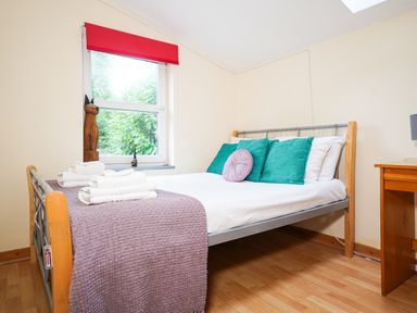 A bedroom with a bed with teal and purple cushions and folded towels near a window with a red blind at Delfryn Goginan in Goginan near Aberystwyth