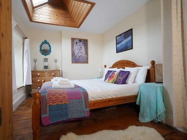 A bedroom with a wooden bed, colorful pillows, a quilt, a wooden dresser, a mirror, paintings, and a skylight at Delfryn, Goginan