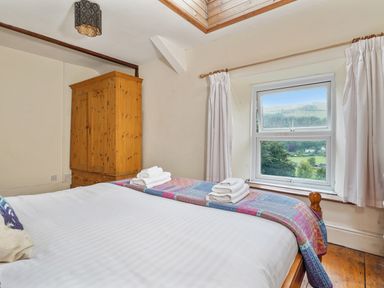 A bedroom with a wooden wardrobe a bed with folded towels and a window with a countryside view at Delfryn Goginan in Goginan near Aberystwyth