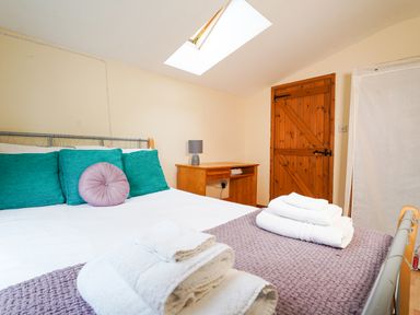 A bedroom with a bed with teal and purple pillows a wooden desk and a wooden door under a skylight at Delfryn Goginan in Goginan near Aberystwyth