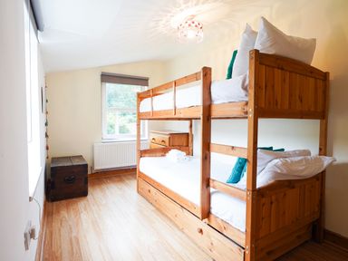A bedroom with wooden bunk beds a chest a window and a radiator at Delfryn Goginan in Goginan near Aberystwyth