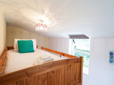 A loft bedroom with a wooden bed frame white bedding and a window with a blind at Delfryn Goginan in Goginan near Aberystwyth