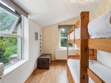 A bedroom with wooden bunk beds a wooden chest and two windows at Delfryn Goginan in Goginan near Aberystwyth