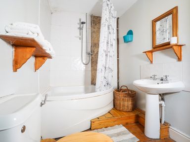 A bathroom with a bathtub and shower a toilet a sink a mirror shelves with towels a wicker basket and a striped rug at Delfryn Goginan Goginan near Aberystwyth