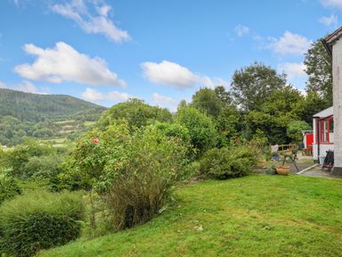 A garden with bushes and chairs next to a house with a mountain in the background at Delfryn Goginan in Goginan near Aberystwyth