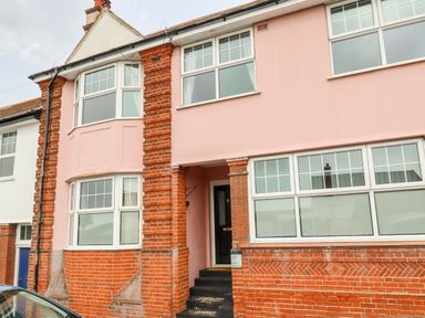 The front exterior of a two-story brick and pink painted house with multiple windows and a black front door at The Pink House in Felixstowe Suffolk