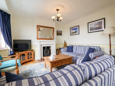 A living room with striped sofas a wooden coffee table a fireplace and a television at The Pink House in Felixstowe Suffolk