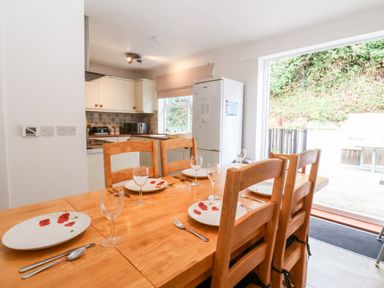 A dining table set with plates and glasses near a kitchen with cabinets and a refrigerator at The Pink House in Felixstowe Suffolk