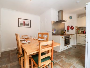 A kitchen with a wooden dining table set with plates and wine glasses next to a cooking area with an oven and stove at The Pink House in Felixstowe Suffolk