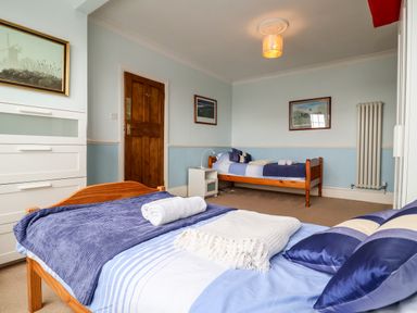 A bedroom with two single wooden beds blue bedding a white chest of drawers and framed pictures on the wall at The Pink House in Felixstowe Suffolk