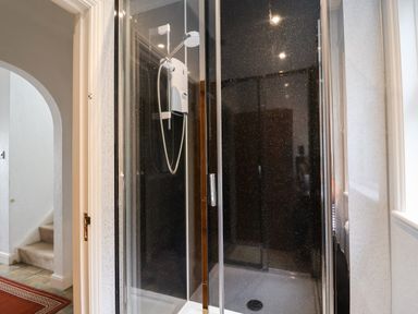 A shower enclosure with black walls and a white shower unit next to a hallway with stairs at The Pink House in Felixstowe Suffolk