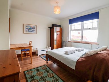 A bedroom with a double bed table and chair a wardrobe a chest of drawers and a window with a blue blind at The Pink House in Felixstowe Suffolk