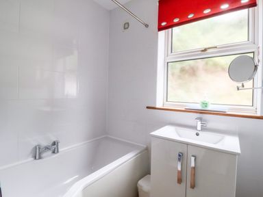 A bathroom with a white bathtub a sink cabinet and a window with a red blind at The Pink House in Felixstowe Suffolk