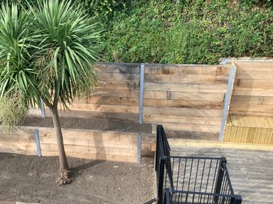 A garden area with a tree wooden retaining walls and a black metal railing at The Pink House in Felixstowe Suffolk