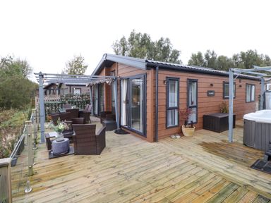 A wooden deck with outdoor furniture and a hot tub attached to a brown cabin at Pine Lake View in Coniston View 3 Carnforth