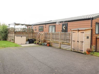 A wooden cabin with a fenced deck and a small shed in an outdoor area at Pine Lake View in Coniston View 3 Carnforth