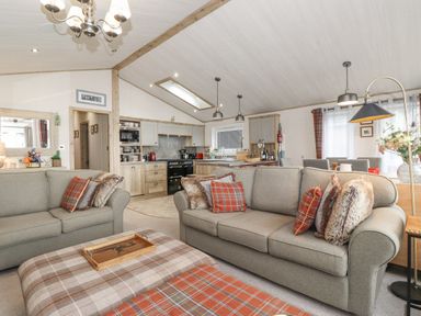 An open-plan living room and kitchen with two sofas and a plaid ottoman at Pine Lake View in Coniston View 3 Carnforth