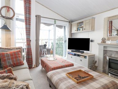 A living room with plaid cushions and ottoman a television and fireplace at Pine Lake View in Coniston View 3 Carnforth