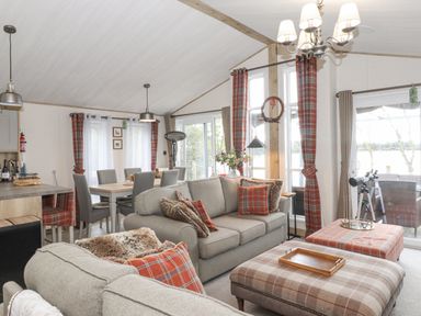 A living room with sofas and plaid cushions next to a dining table with grey chairs at Pine Lake View in Coniston View 3 Carnforth