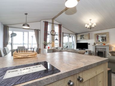 An open living room and kitchen with a countertop view showing a sofa a fireplace a television and windows with curtains at Pine Lake View Coniston View 3 Carnforth