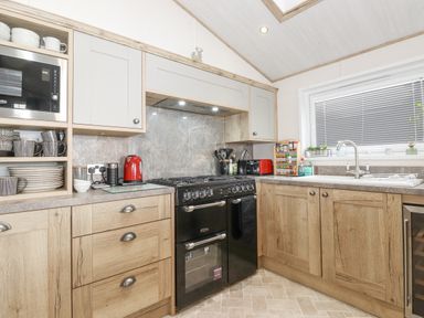 A kitchen with wooden cabinets a black oven a microwave dishes and cups on shelves at Pine Lake View in Coniston View 3 Carnforth
