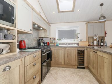 A kitchen with wooden cabinets a microwave red kettle stove and oven and a window with blinds at Pine Lake View in Coniston View 3 Carnforth