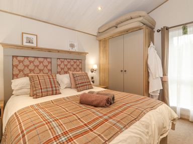 A bedroom with a double bed pillows and plaid bedding next to a wardrobe with cushions on top at Pine Lake View in Coniston View 3 Carnforth