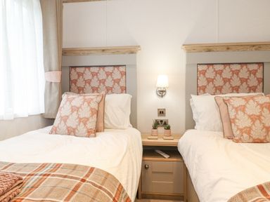A bedroom with two single beds separated by a nightstand and a wall lamp at Pine Lake View Coniston View 3 Carnforth