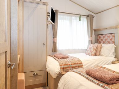A bedroom with two single beds a wardrobe a wall-mounted television and a window with curtains at Pine Lake View Coniston View 3 Carnforth