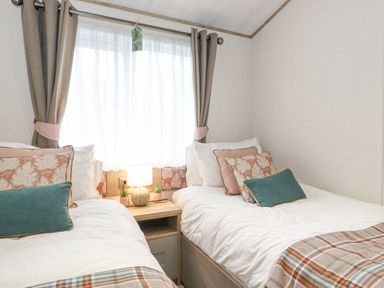 A bedroom with two single beds a nightstand with a lamp and curtains on the window at Pine Lake View in Coniston View 3 Carnforth