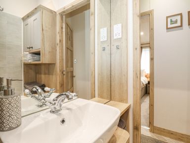 A bathroom sink with a faucet and soap dispenser next to a wooden cabinet and doorway showing part of a bedroom at Pine Lake View Coniston View 3 Carnforth