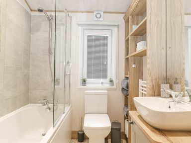 A bathroom with a bathtub shower combination a toilet a wooden shelf unit with towels and a sink at Pine Lake View in Coniston View 3 Carnforth