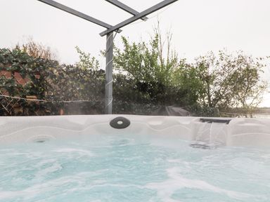 A hot tub with water flowing and bubbles outside near greenery at Pine Lake View Coniston View 3 Carnforth