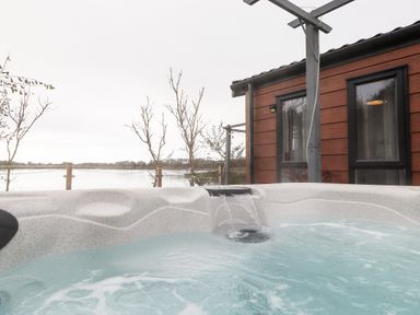 A hot tub with water flowing into it outside a building with windows near a lakeside view at Pine Lake View in Coniston View 3 Carnforth