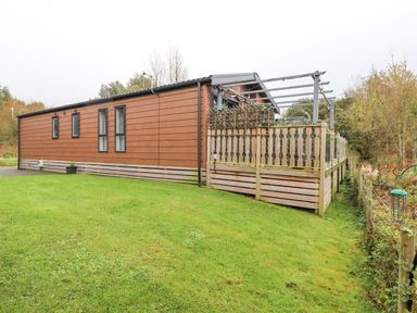 A brown mobile home with multiple windows and a wooden fenced deck on a grass lawn at Pine Lake View in Coniston View 3 Carnforth
