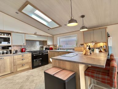 A kitchen with wooden cabinets a black oven a skylight and a countertop with bar stools at Pine Lake View in Coniston View 3 Carnforth