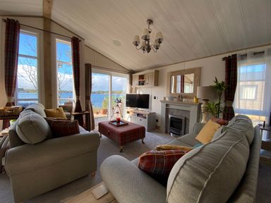 A living room with sofas a television and a fireplace overlooking a lake at Pine Lake View in Coniston View 3 Carnforth
