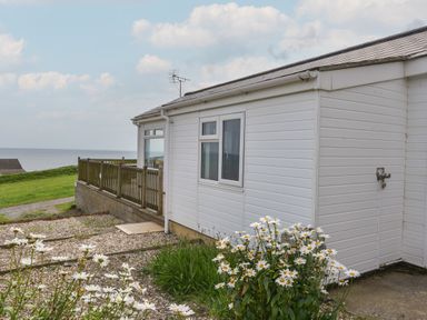 Exterior of a white building with a wooden fence overlooking the sea and flowers in the foreground at Sealark in Eype
