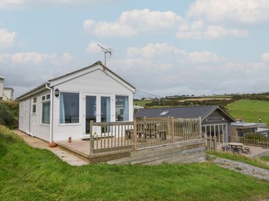 A small white house with a wooden deck and railing overlooking green hills at Sealark in Eype