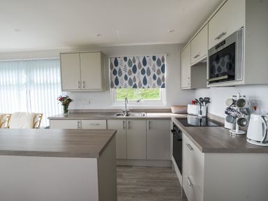 A kitchen with light cabinets a double sink a microwave oven and a coffee cup holder at Sealark in Eype