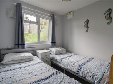 A bedroom with two single beds a window with curtains and a white bedside cabinet at Sealark in Eype
