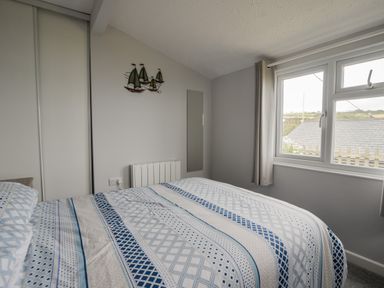 A bedroom with a bed covered in patterned blue and white bedding and a window with curtains at Sealark in Eype