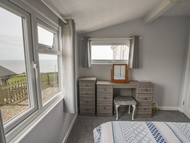 A bedroom corner with a wooden dressing table a cushioned stool and windows with curtains showing an outdoor view at Sealark in Eype