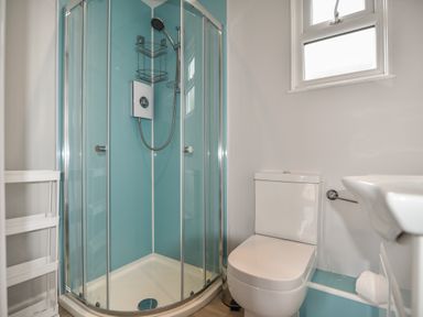 A bathroom with a shower enclosure a toilet a window and a sink at Sealark in Eype