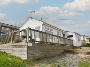 A white caravan with a wooden deck and railing on a grassy and gravel area at Sealark in Eype